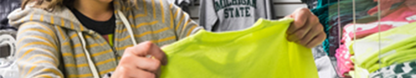 A woman holds and examines a Michigan State t-shirt in the shop.msu.edu storefront